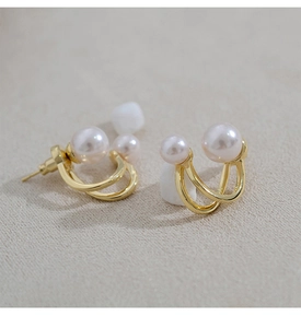 Macro detail of elegant gold double-loop pearl earrings featuring smooth metallic textures