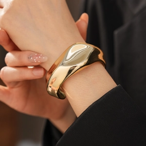 Close-up of a wide gold cuff bracelet featuring irregular wavy design and polished finish