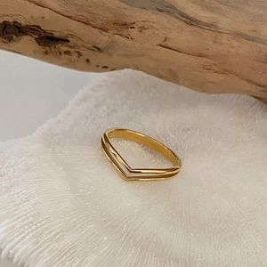 Detail shot of 18K gold double-layered V-shape ring on a white textured stand