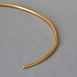 Macro shot of minimalist gold-plated collar necklace featuring polished brass and smooth ends