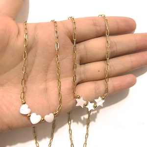 Gold paperclip chain necklace with white heart and star shell pendants in hand