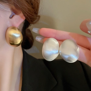 Detail of matte gold and silver geometric oval chunky earrings with brushed metal finish