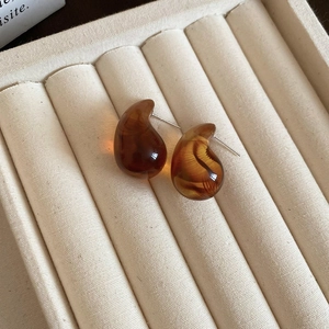 Macro detail of amber resin teardrop earrings with silver needles on a velvet tray