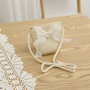 Detail of a beige straw crossbody bag with white organza bow and pearl for girls