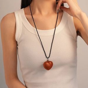 Détail d'un pendentif cœur en cuir marron avec couture tressée sur collier cordon noir