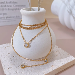 Detail of layered gold stainless steel necklace with round zircons on a ceramic vase
