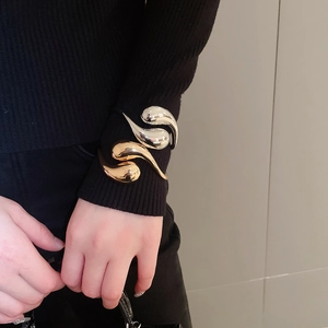 Macro detail of stacked gold and silver teardrop bangles over a black knit sleeve