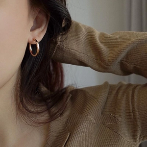 Close-up of minimalist rose gold hoop earrings worn by a model in warm lighting