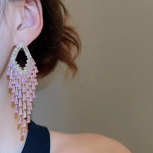 Detailed view of long gold fringe earrings with pink geometric rhinestones on a model