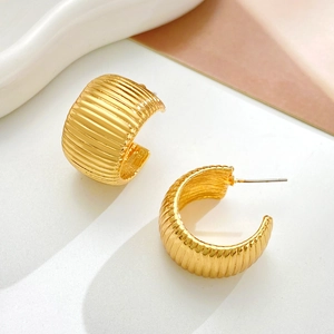Macro detail of wide gold C-shape earrings with a ribbed texture and metallic finish
