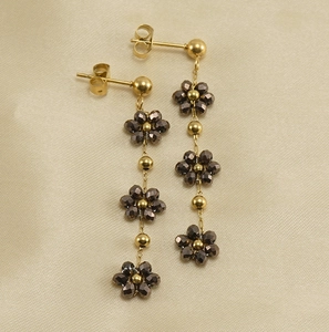 Close-up of golden beaded drop earrings with dark crystal flower charms on beige fabric