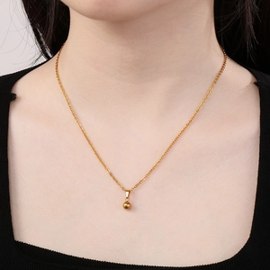 Close-up of minimalist gold bead pendant necklace worn by model on black neckline