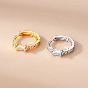 Macro detail of gold and silver huggie hoop earrings with rectangular zircon inlay