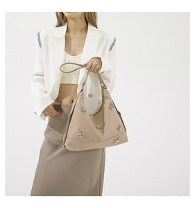 Detail of beige shoulder bag featuring decorative silver bow metal hardware and leather strap