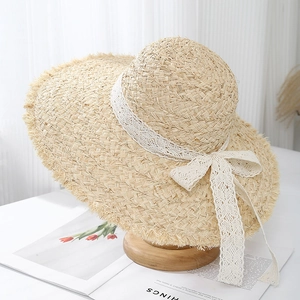 Close-up of raffia sun hat featuring white lace ribbon bow and frayed wavy brim detail