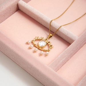 Detail of gold evil eye necklace with white zircon and pearls in pink velvet box