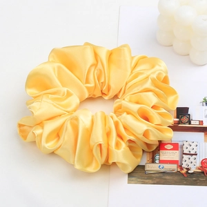 Close-up of light yellow satin scrunchie with silky texture and elegant folds on white background
