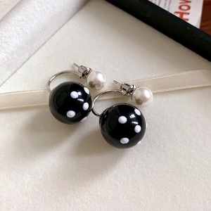 Macro view of black acrylic C-shaped earrings with white polka dots and pearl backings