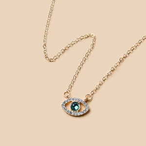 Close-up of a gold Evil Eye pendant necklace featuring a green crystal and white diamonds