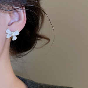 Detail view of cream enamel bow stud earring with white zircon inlay on model
