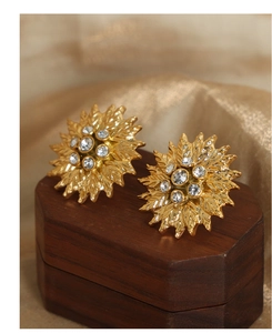Macro detail of gold flower earrings with zircon centers on a luxury wooden box