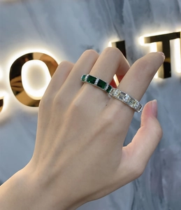 Detailed view of an emerald cut green gemstone and silver eternity ring on a hand