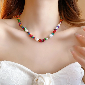 Detail of colorful stone and baroque pearl necklace worn by a model in warm light