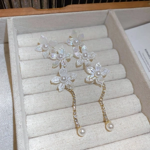 Detailed close-up of lily flower earrings with pearl tassels on a jewelry display tray