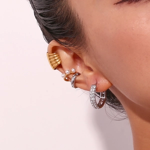 Detail of layered gold and silver earrings including pearl cuff and micro-set hoop earrings