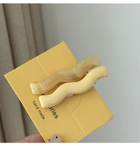 Close-up of wavy resin hair clips in beige marble and pale yellow on display card