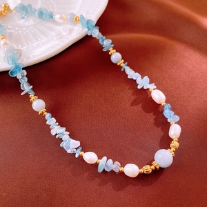 Close-up of aquamarine stones and freshwater pearls on a gold-beaded necklace