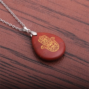 Detail of red teardrop stone pendant with golden Hamsa Hand on a silver chain