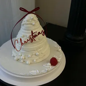 Christmas tree-shaped cream cake with white pearls, red ribbon bow, and festive topper