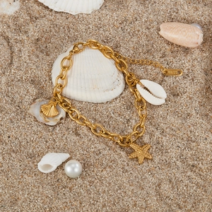 Detailed shot of gold stainless steel bracelet with starfish and shell charms on beach