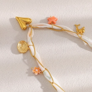 Detail van 18K gouden ketting met wit lint en bedeltjes in zeethema zoals schelpen