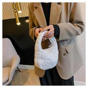 Close-up of white quilted mini cloud bag held by a model in a brown blazer suit
