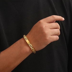 Golden Byzantine chain bracelet with rectangular plate worn on wrist against black background