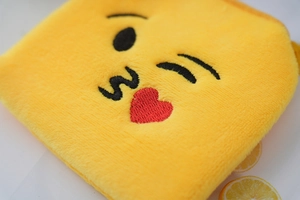 Macro shot of yellow plush coin purse with wink and kiss emoji embroidery detail