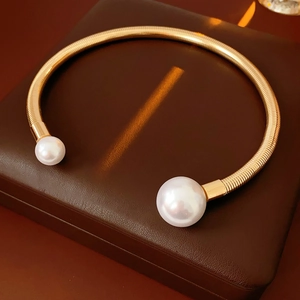 Close-up of a gold metal choker necklace with elegant white pearls on a leather box