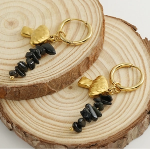 Detail of 18k gold mushroom earrings with black natural stone tassels on wood background