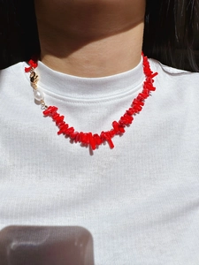 Detail of a red coral stone necklace with a baroque pearl worn on a white sweater