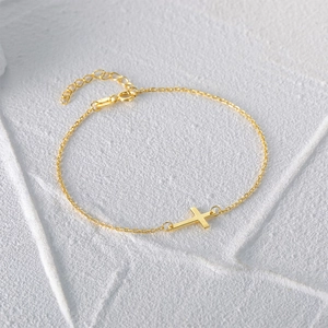 Detailed macro view of a gold-plated cross bracelet with adjustable lobster clasp closure