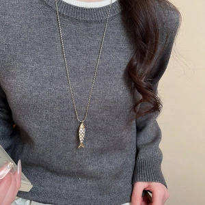 Detail of fish pendant on gold chain with white shell scales over dark grey knitwear