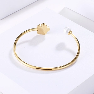 Detail of gold floral open cuff featuring a white pearl and polished clover charm
