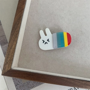 Close-up of a white acrylic rabbit hair clip with colorful stripes on a wooden base