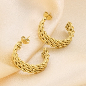 Detail of twisted gold C-shaped earrings on elegant champagne satin fabric