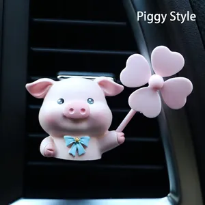 Detail of pink pig car vent clip with a blue bow and windmill on a black air vent