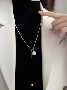 Detail of elegant Y-shaped gold snake chain necklace with white pearl and metal bead