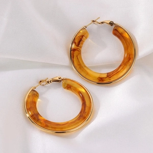 Détail de boucles d'oreilles en résine ambre écaille sur fond de soie blanche