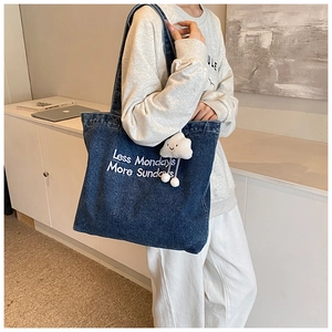 Detail of navy denim tote bag with white embroidery and a cute cloud plush keychain accessory